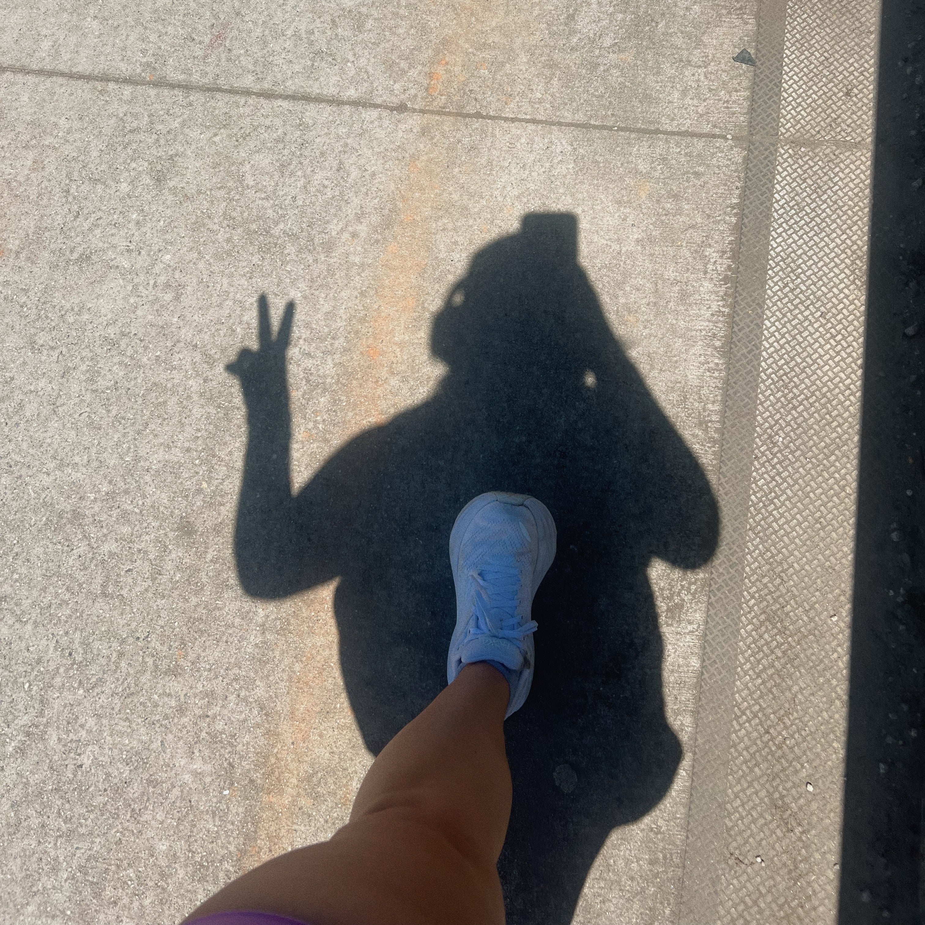 Shadow of a person making a peace sign on a concrete surface with a blue shoe visible.