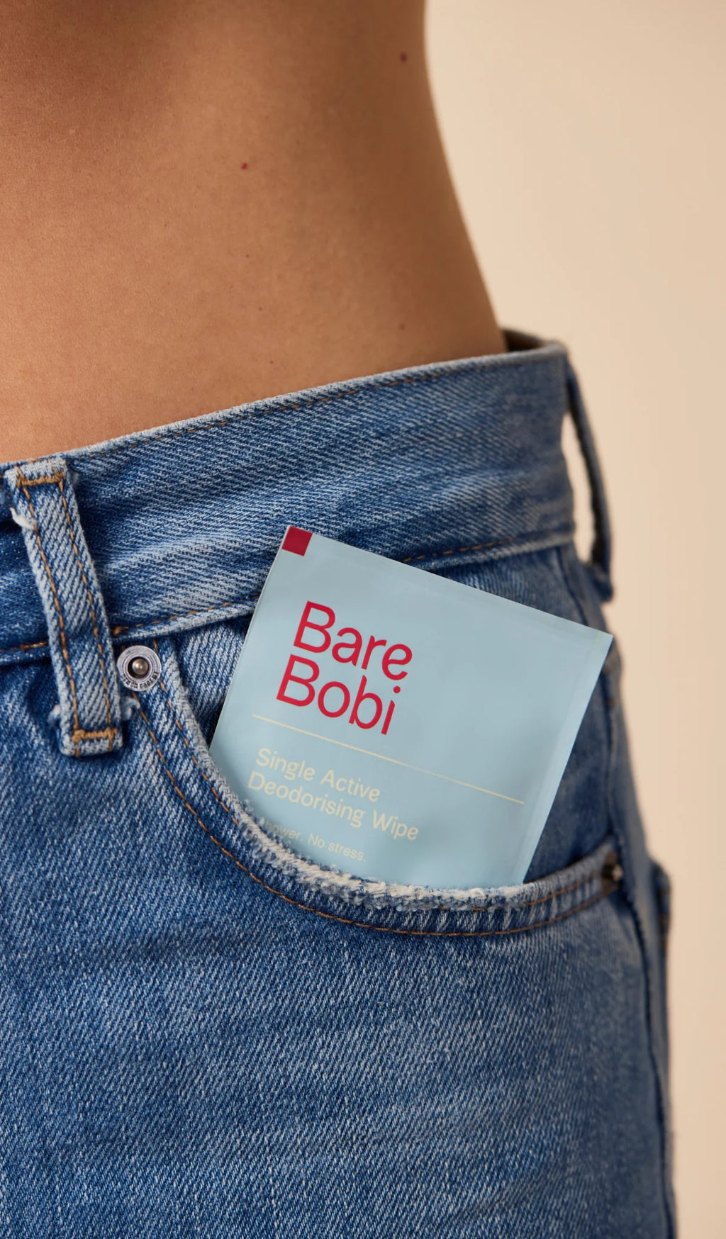 Person wearing blue jeans with a 'Bare Bobi' product in the pocket against a beige background
