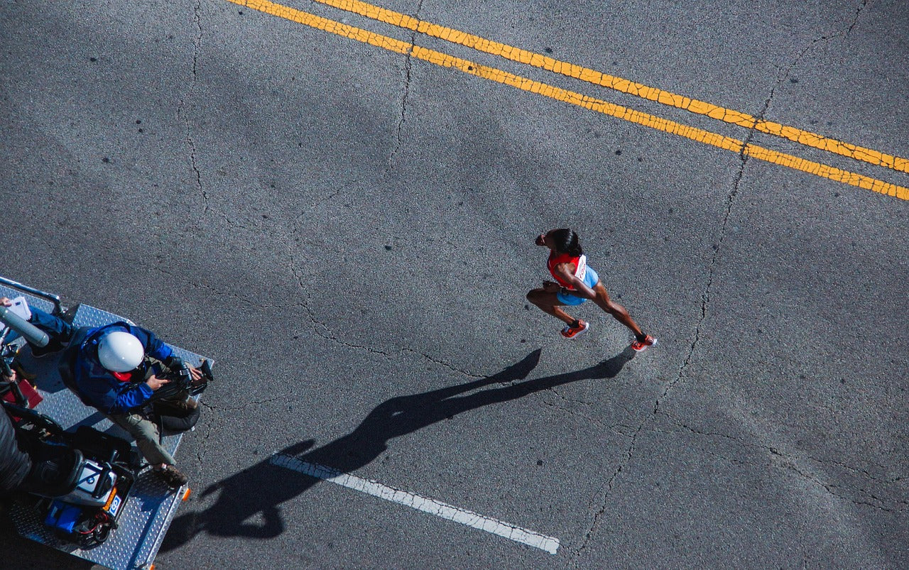 Woman running on a road with yellow dividing lines, viewed from above.